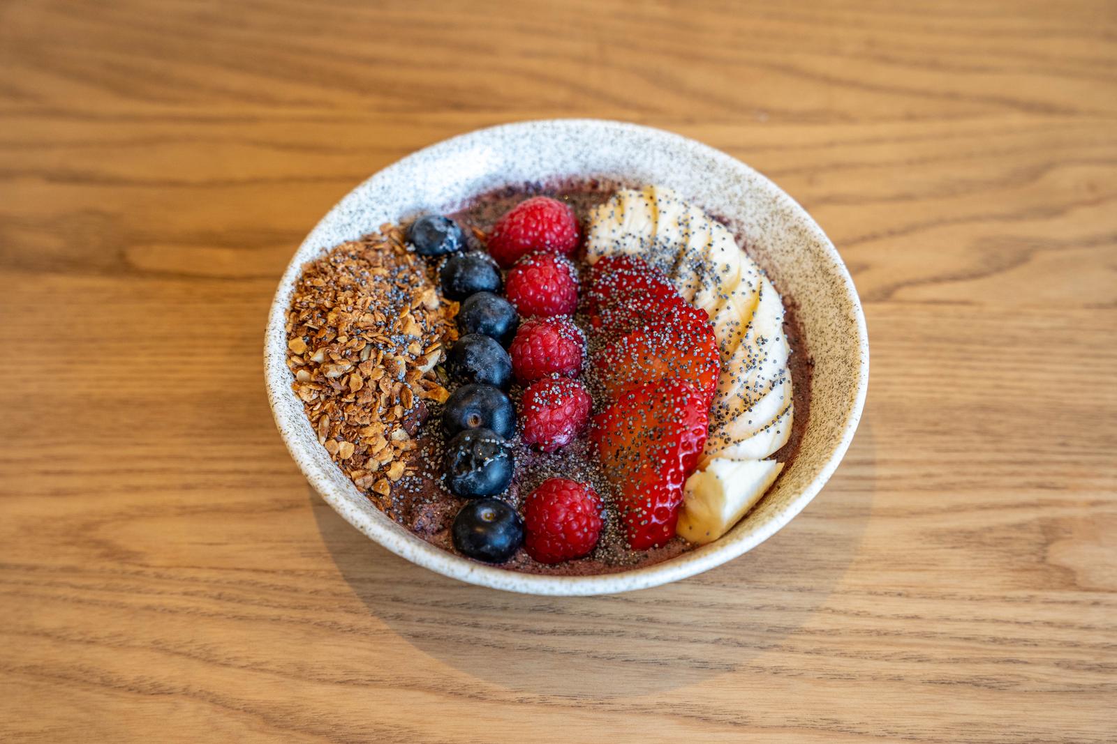 Bol d'açaí amb fileres de granola, nabius, gerds, maduixes, plàtan i llavors de chía.