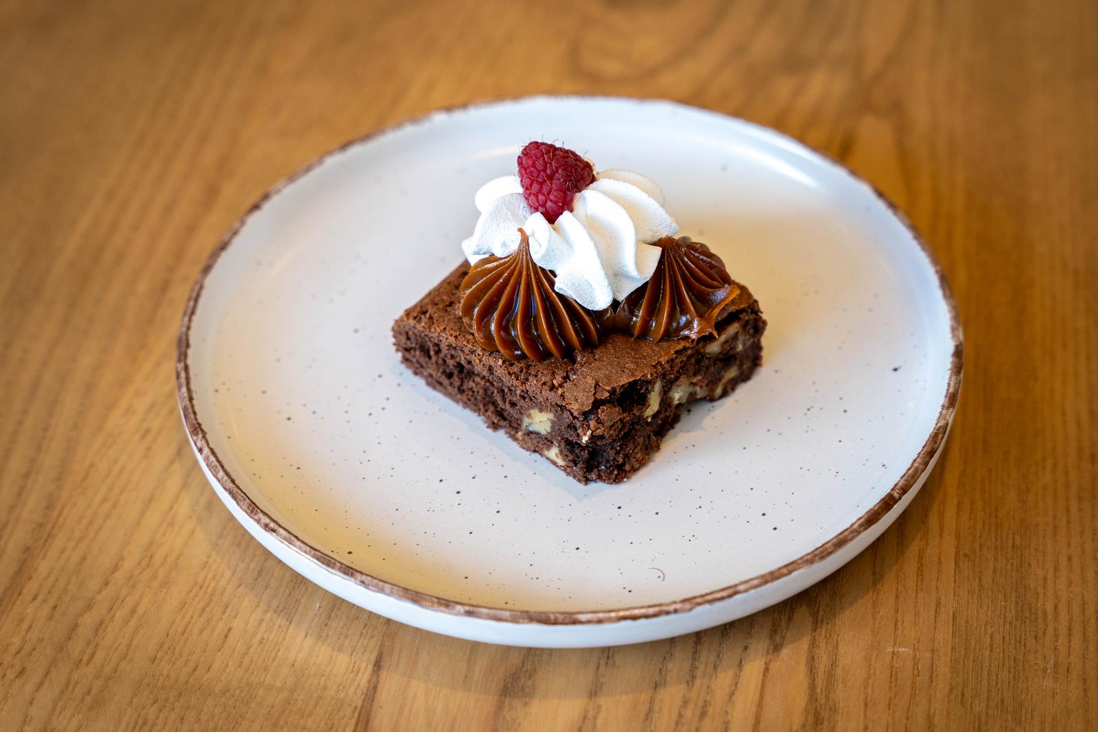 Porció de brownie amb nous, crema de xocolata, nata muntada i un gerd sobre plat blanc.