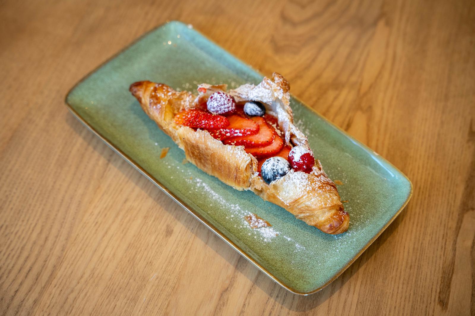 Croissant obert farcit de maduixes, nabius i gerds amb sucre glas sobre safata verda.