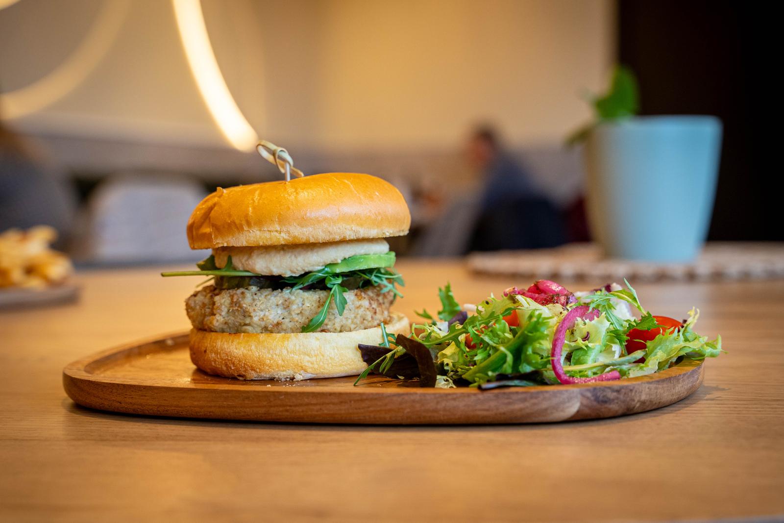 Hamburguesa de pollastre arrebossat amb rúcula en pa de brioix i amanida, sobre taula de fusta al local.
