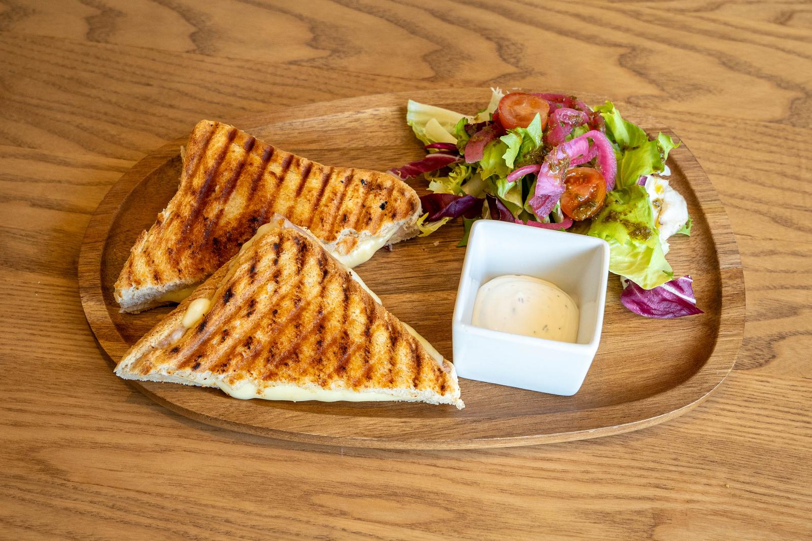 Dos triangles de panini torrat amb formatge fos, amanida i salsa sobre taula de fusta.