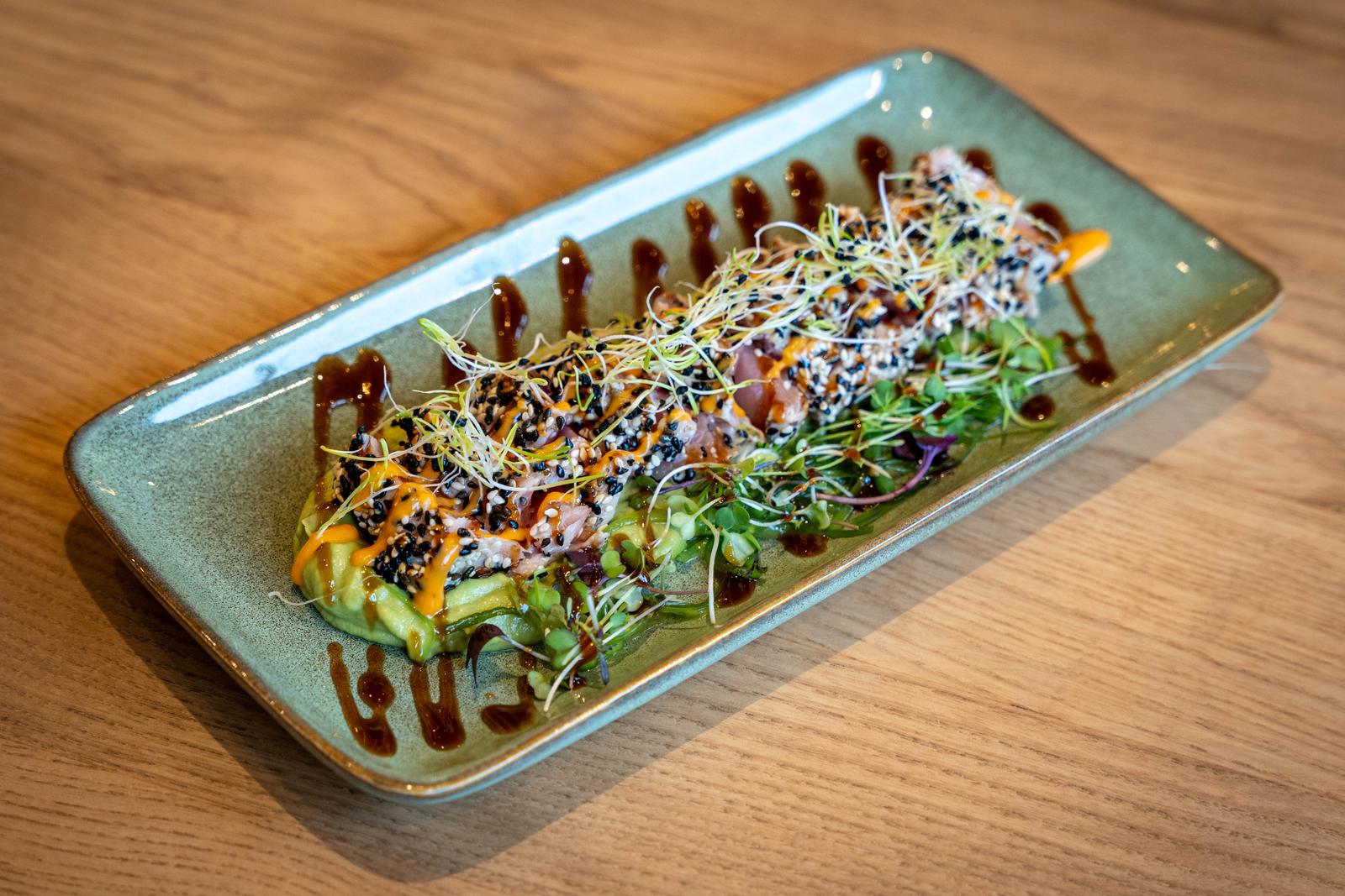 Tataki de tonyina segellada amb sèsam sobre crema d'alvocat, brots i salsa teriyaki en safata allargada.
